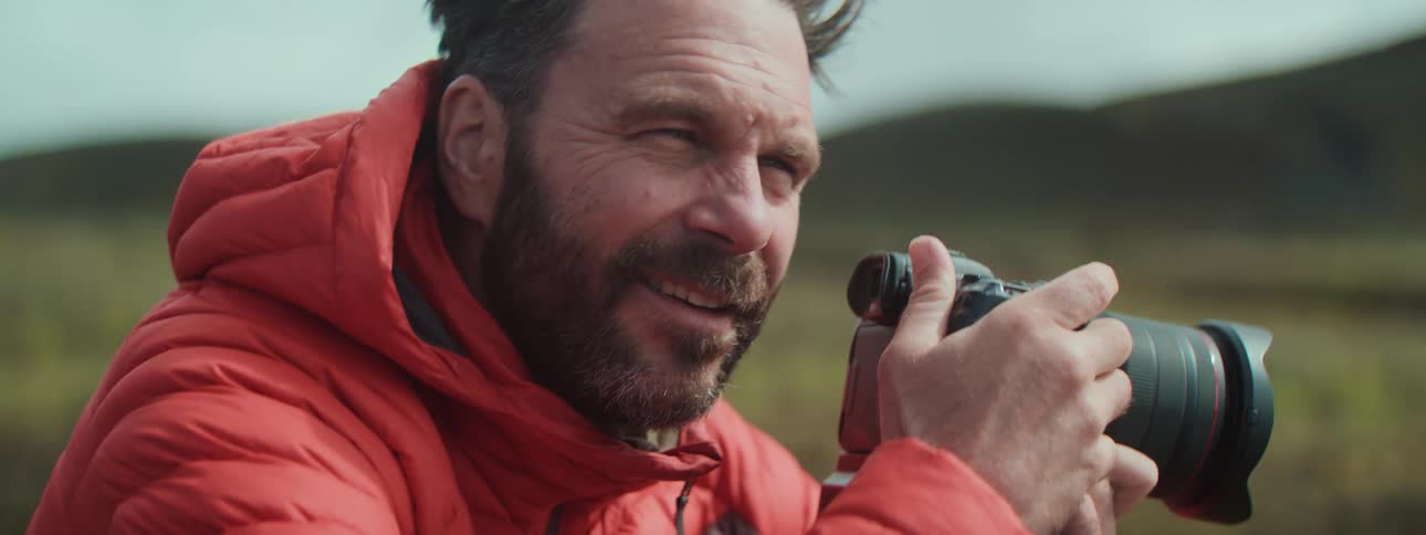 Slow motion close-up of a smiling, bearded photographer in a red jacket enjoying taking pictures in nature