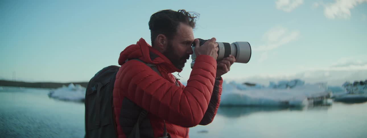 A dedicated photographer in a red jacket focuses his camera on a beautiful glacial lagoon