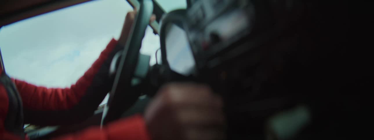 An artistic and blurry point-of-view shot from inside a car showing the driver's hands steering and shifting gears on a road trip