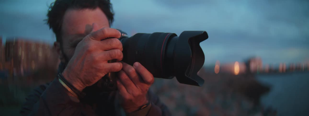Close-up of a focused male photographer taking pictures with a professional camera during sunset