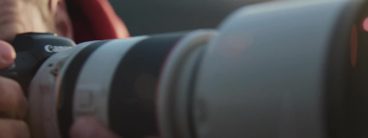A cinematic slow-motion close-up reveals a photographer holding a professional camera with a telephoto lens