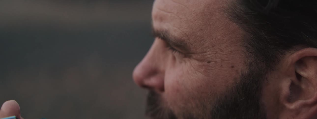 An extreme close-up shot captures a pensive bearded man slowly closing his eye