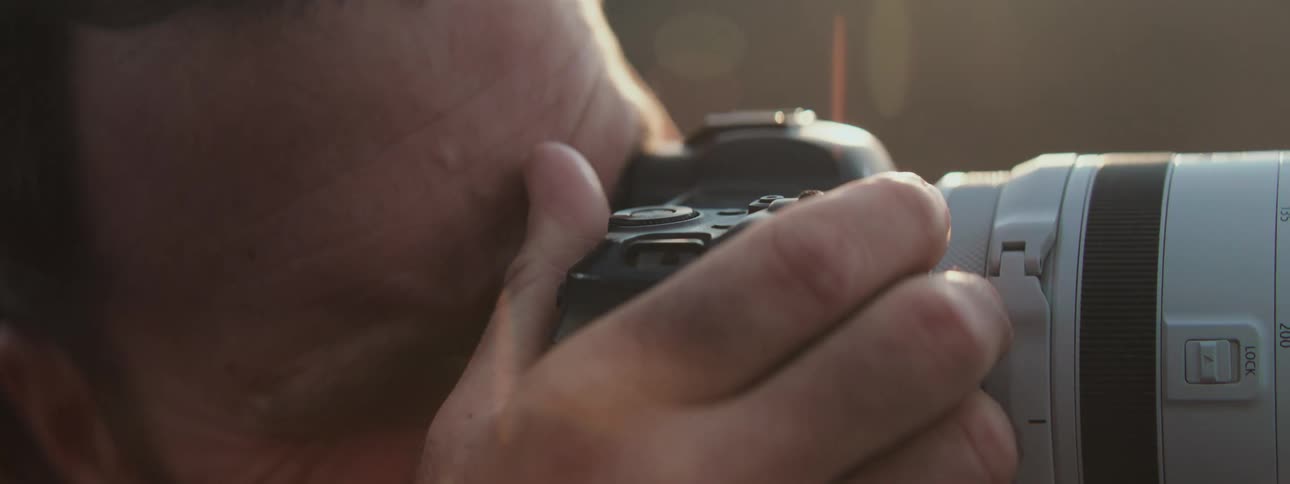 A close-up shot of a photographer adjusting the controls and looking through the viewfinder of a camera during golden hour