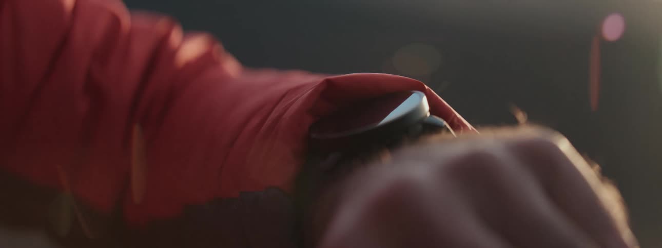 A cinematic close-up of a man's wrist reveals a smartwatch with a beautiful sun flare in the background