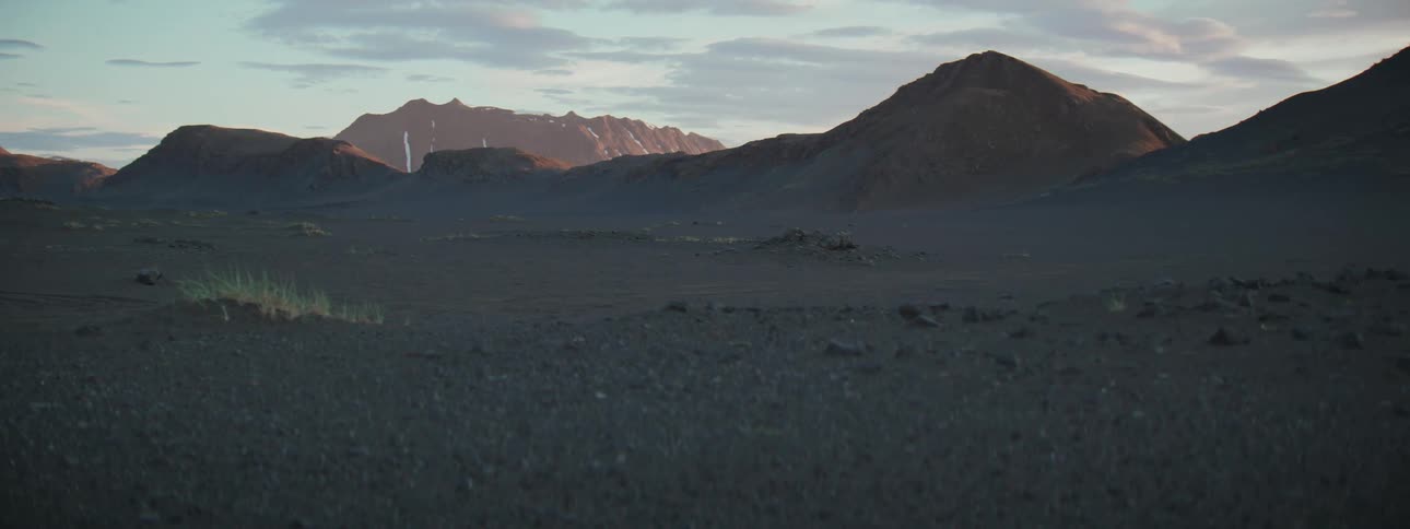 Golden hour light illuminates distant snow-capped mountains across a vast, dark volcanic landscape