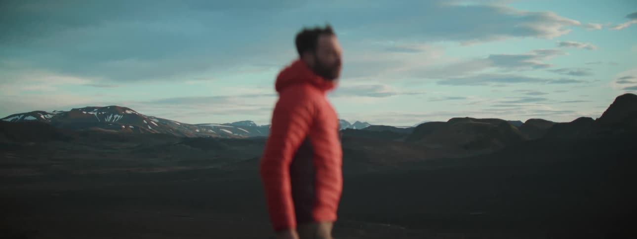 A stunning wide shot of a vast mountainous landscape with a man in a red jacket out of focus in the foreground