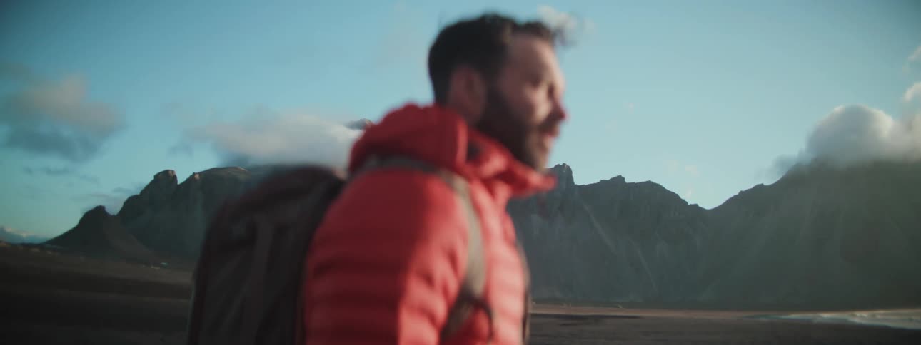 A man wearing a red jacket and backpack hikes through a vast mountain landscape at sunrise