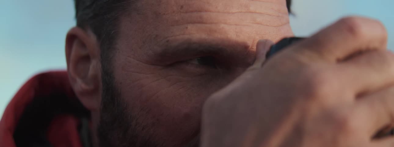 Extreme close-up on the face of a thoughtful, bearded photographer as he looks through his camera's viewfinder