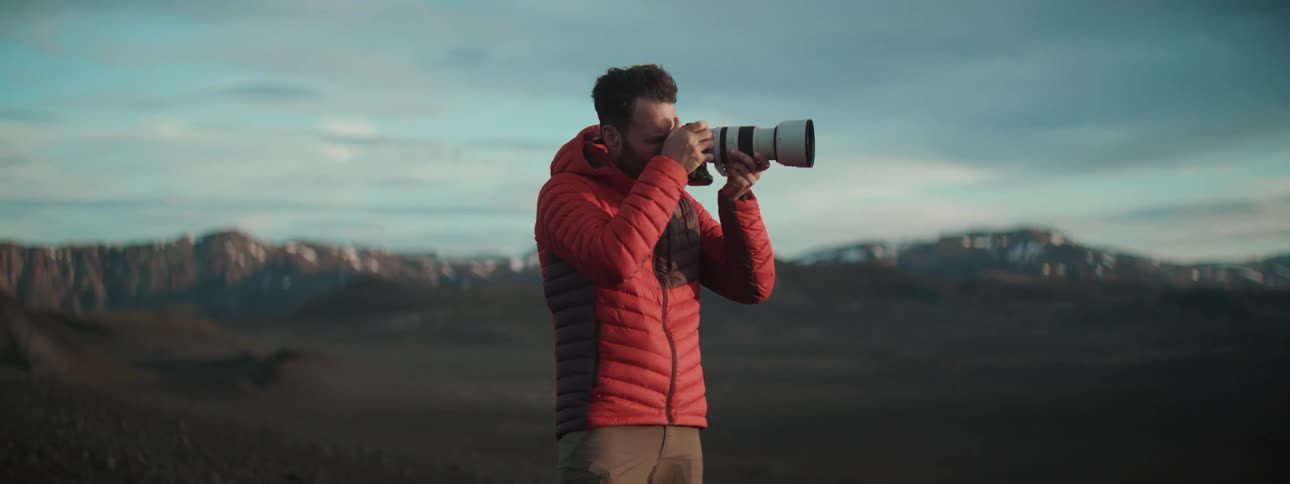 A professional photographer in a red jacket captures the stunning mountain landscape with a telephoto lens
