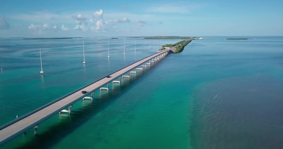 Cars travel on a long bridge spanning blue ocean