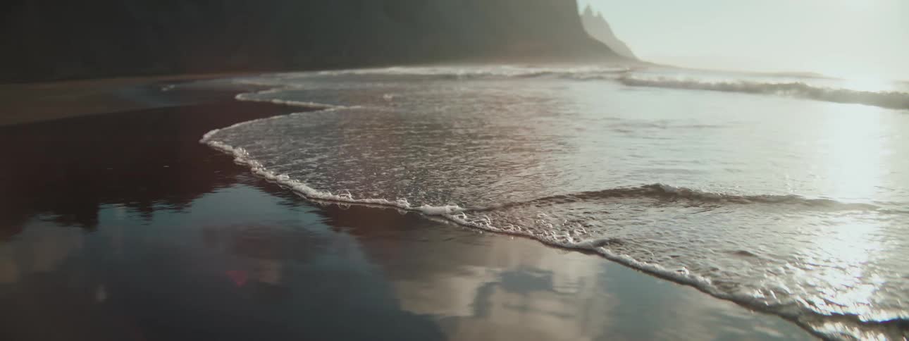A peaceful, slow-motion close-up of gentle waves washing up on a reflective, wet sand beach