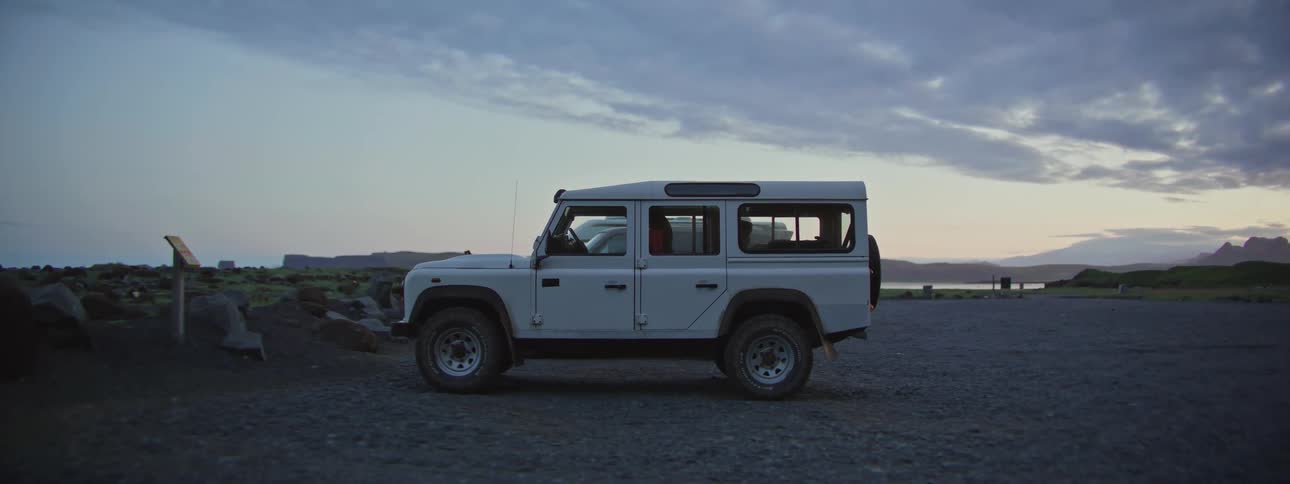 A white off-road vehicle sits parked in a remote gravel lot during the twilight hours