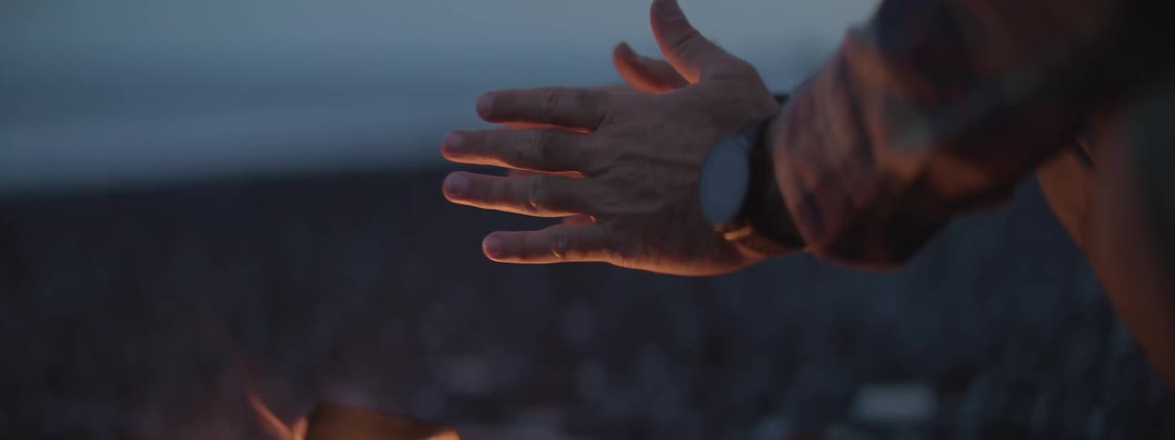 Close up of a man's hands illuminated by the warm glow of a campfire at dusk