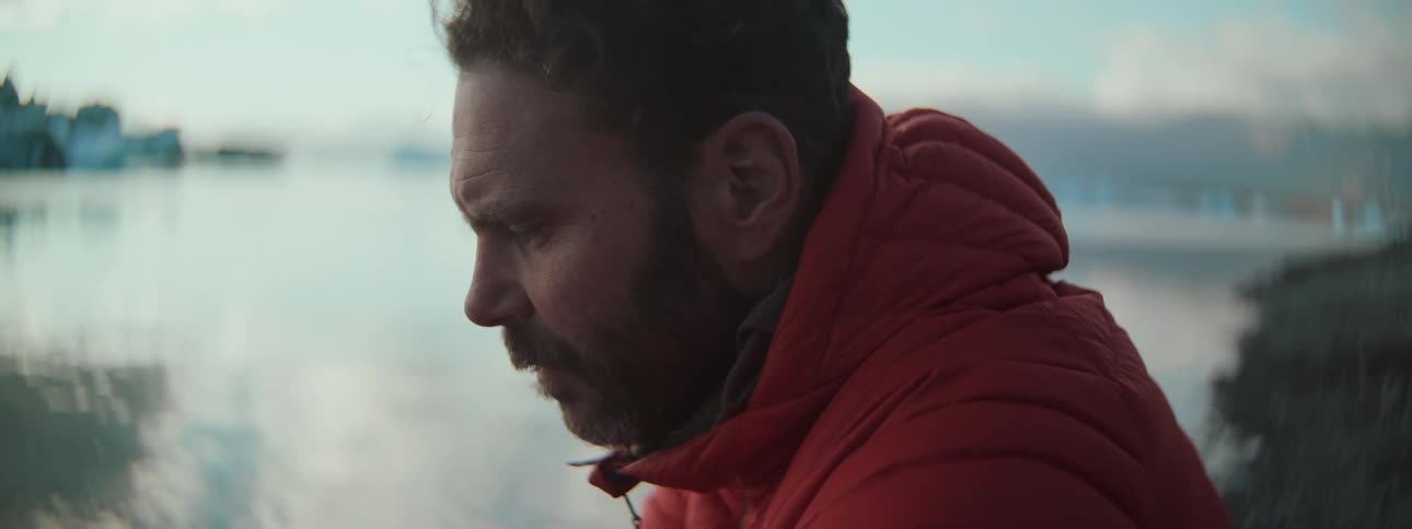 Close-up profile of a thoughtful man in a red winter coat contemplating by the water