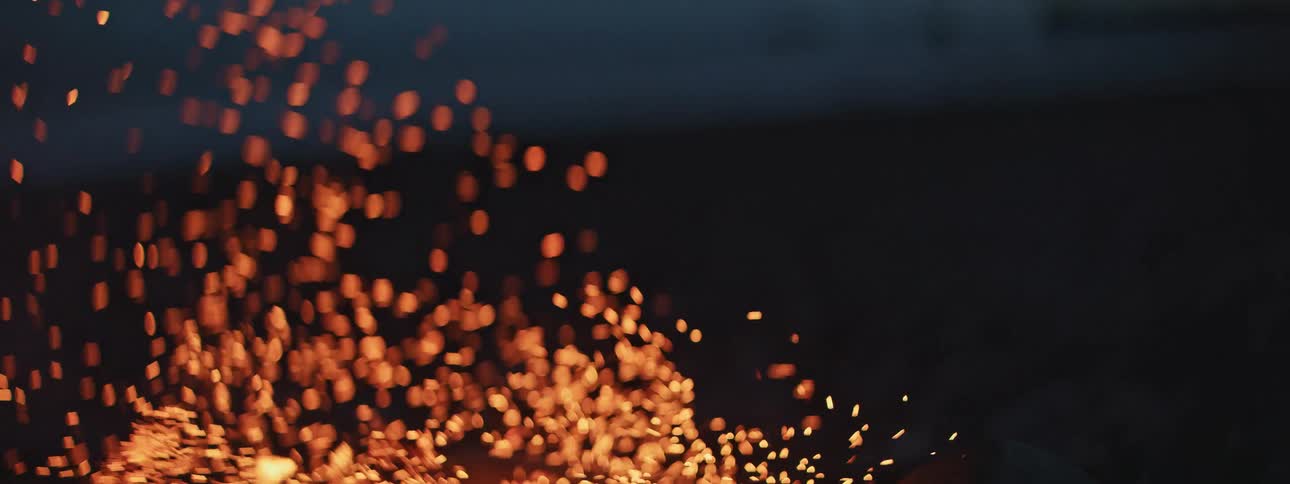 Slow motion shot of glowing embers and sparks rising from a bonfire against the dark night sky