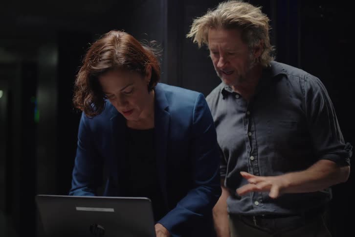 Two IT specialists, a man and a woman, troubleshoot a problem on a laptop in a server corridor