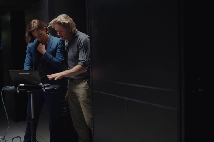 An IT professional explains server data to a businesswoman on a laptop in a secure data center
