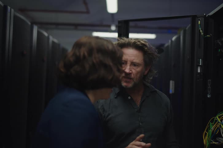 A male and female IT professional collaborate and discuss technical issues while working in a server room