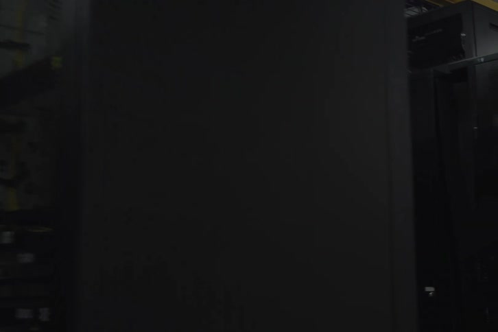 A slow pan reveals rows of black server racks with blinking lights in a dark, modern data center