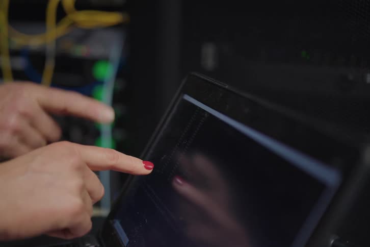 IT technicians collaborate in a server room, diagnosing a network issue on a laptop before checking the server rack