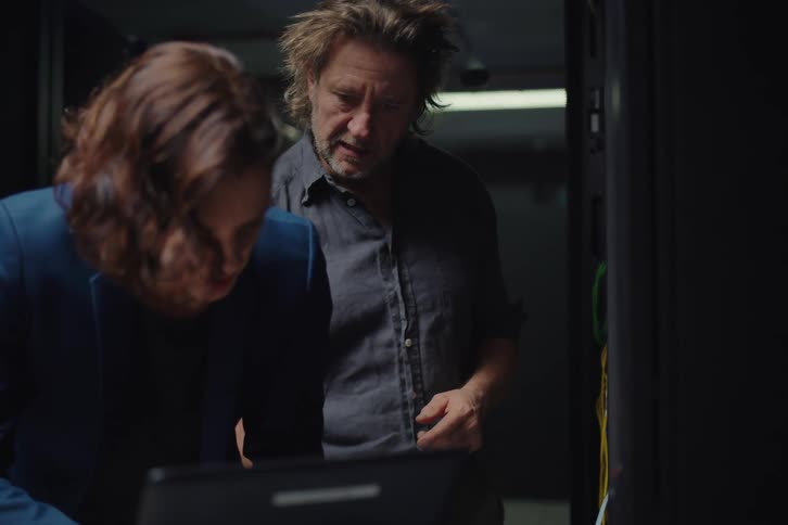 A male technician assists a female IT administrator as she diagnoses a server issue on her laptop in a dark data center