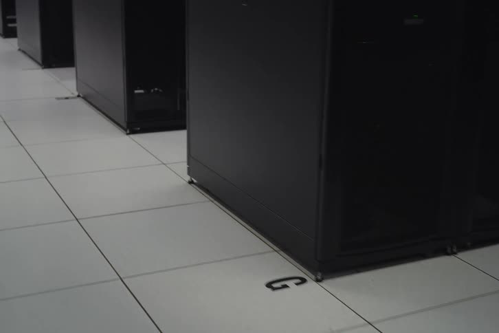 A slow dolly shot moves along the tiled floor of a modern data center, passing rows of black server racks
