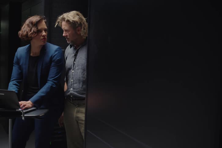 A male and female IT engineer discuss data on a laptop while working in a server room