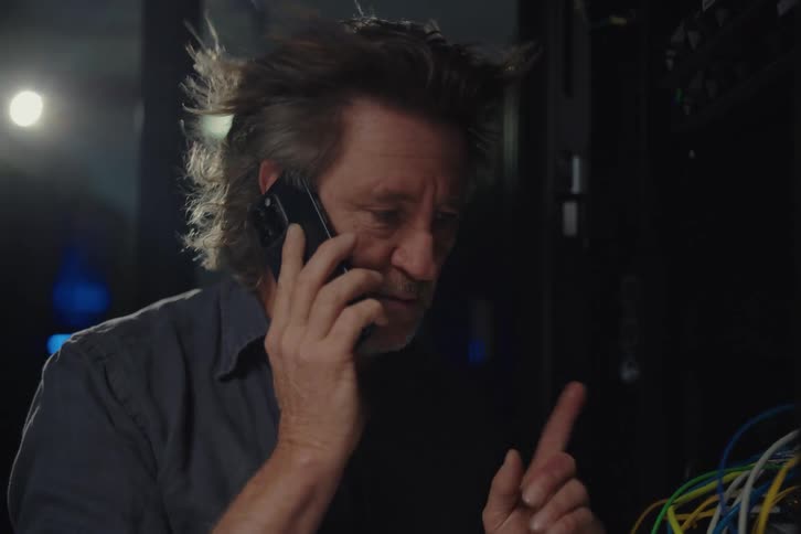 A stressed IT technician in a server room talks on the phone while trying to solve a network problem