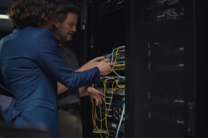 A male IT technician explains the network server cabinet wiring to a female manager in a modern data center