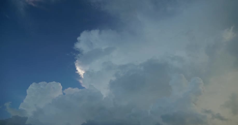 A view of a blue sky with white and dark clouds moving around