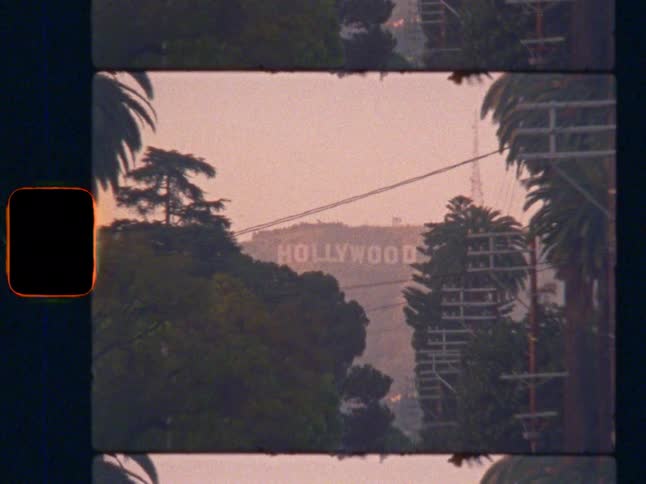 Zoom out from the iconic Hollywood sign to reveal a palm tree-lined Los Angeles street at dusk, on nostalgic Super 8 film