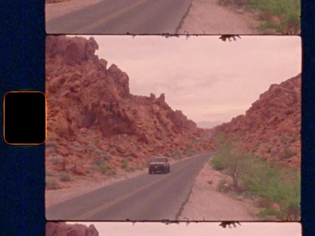 An SUV driving down a scenic road through a red rock canyon, on Super 8 film
