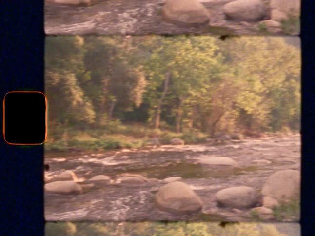A Super 8 film shot pans across a beautiful, flowing river surrounded by lush green trees and rocks