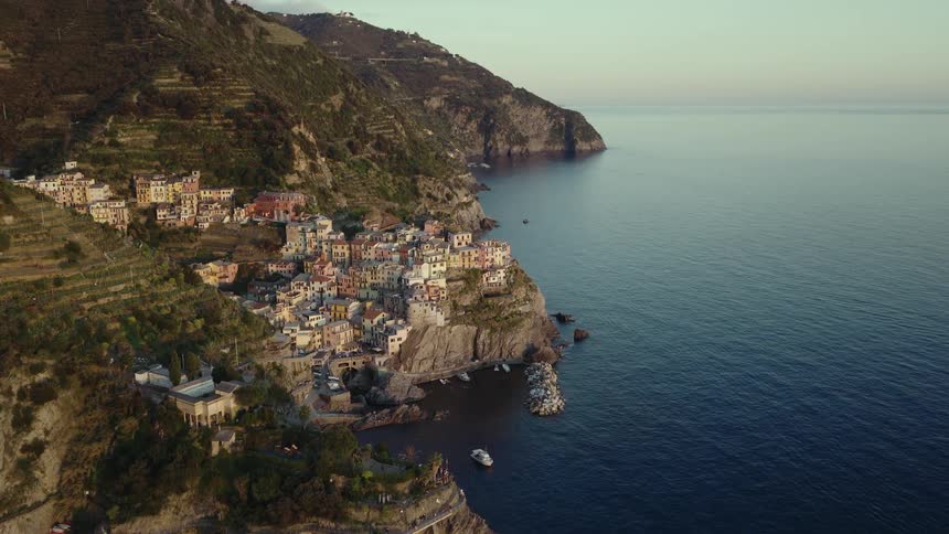 A stunning aerial view captures the picturesque coastal village of Manarola in Cinque Terre, Italy, as a train passes by along the cliffside at sunrise