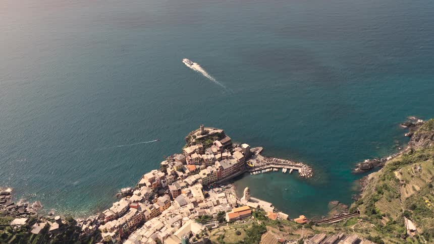 A breathtaking aerial shot zooms towards the historic coastal village of Vernazza in Italy's Cinque Terre, as a boat sails across the blue sea