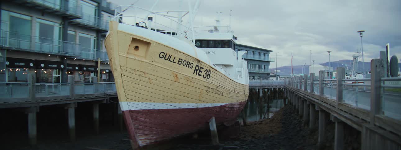 A weathered fishing trawler named Gullborg is beached in a harbor at low tide