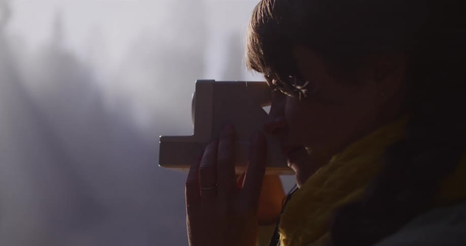 A young woman in a yellow scarf smiles and takes a picture with a vintage instant camera as beautiful sun rays pierce through the morning mist