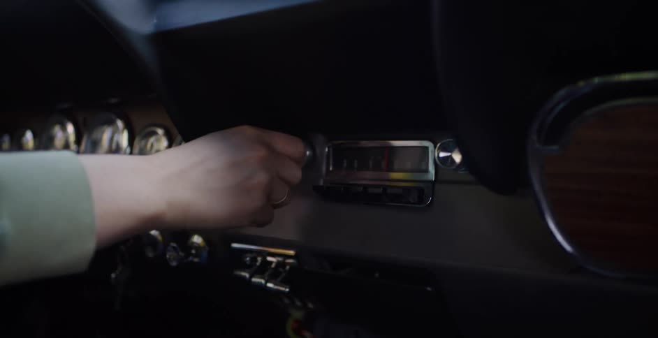 Close up of a driver's hand tuning the classic analog radio on the dashboard of a vintage car