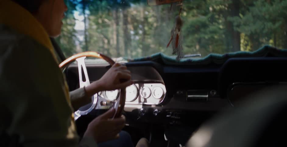 Interior shot of a person driving a classic car down a scenic forest road on a sunny day