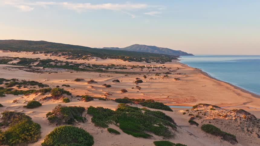 Stunning aerial footage captures the vast golden sand dunes meeting the tranquil blue sea along a picturesque coastline at sunset