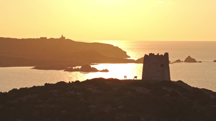 A ruined coastal watchtower is silhouetted against a brilliant golden sunset over the Mediterranean Sea