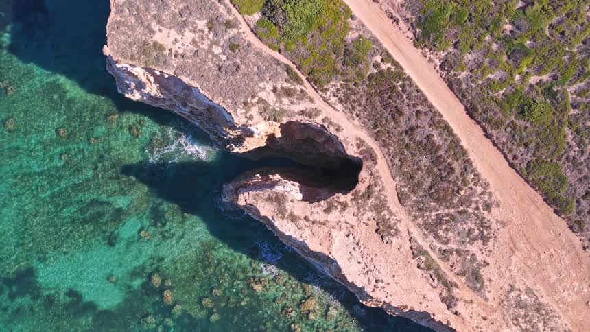 A breathtaking aerial top-down shot slowly pulls away from a natural sea cave, revealing the turquoise ocean and rugged coastline