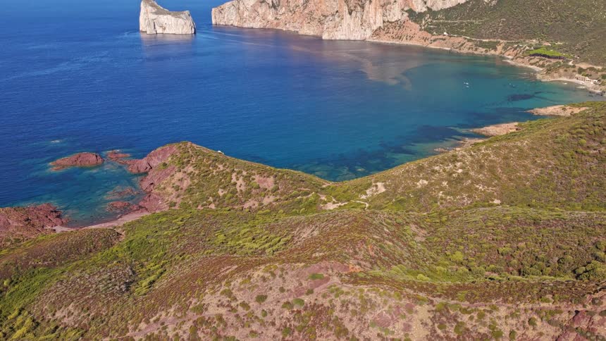 An aerial drone shot slowly reveals the stunning Pan di Zucchero sea stack and the turquoise waters of Porto Flavia on the coast of Sardinia, Italy