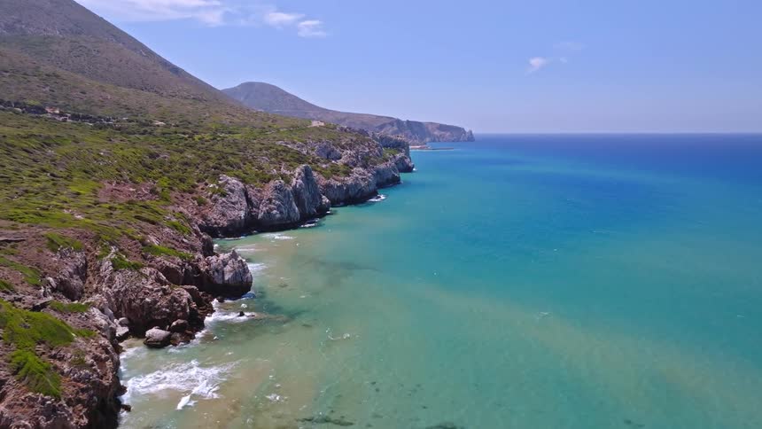 An epic aerial view flies along a beautiful, rugged coastline with turquoise water on a clear sunny day