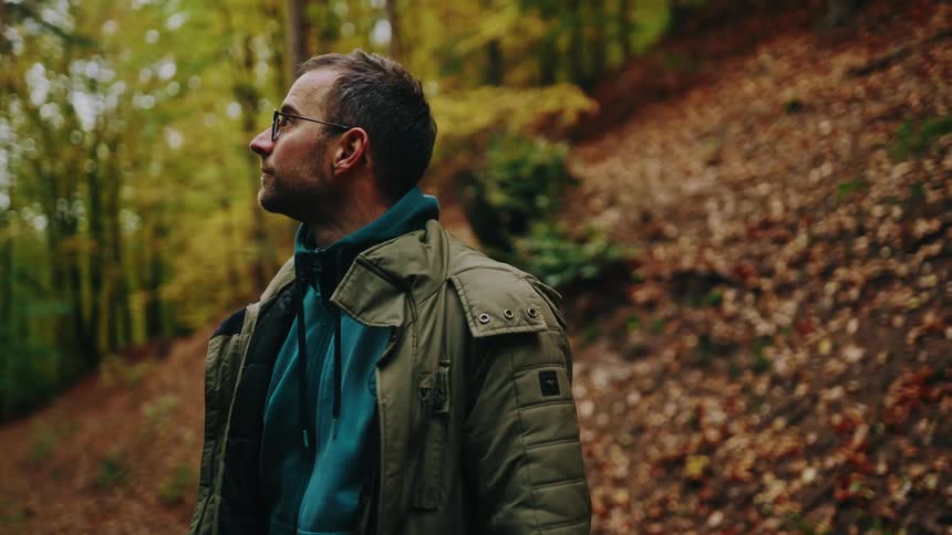 A contemplative man wearing glasses takes a moment to admire the tranquil beauty of a vibrant autumn forest