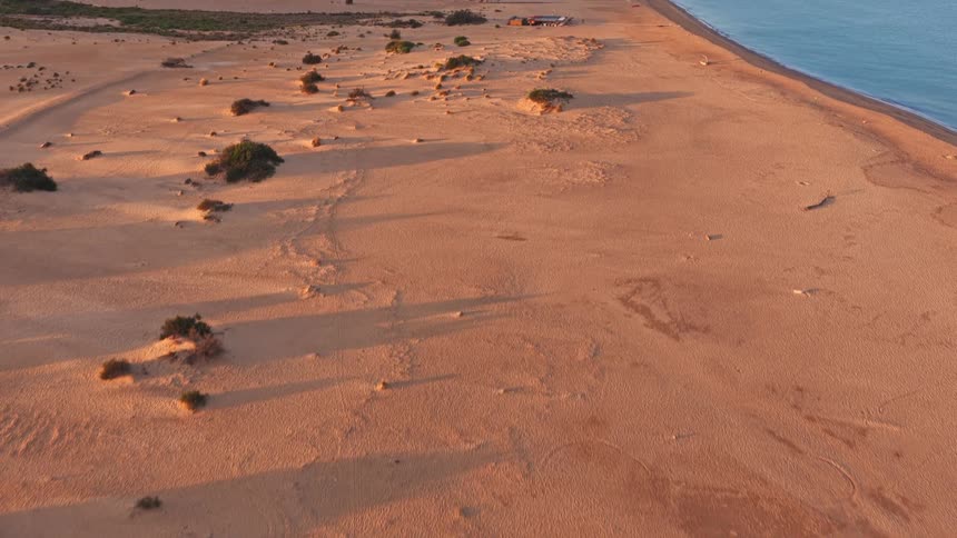 An aerial journey from a desert oasis over vast sand dunes to the beautiful blue ocean at sunrise