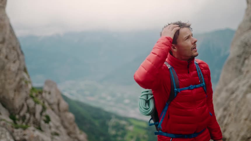A determined male mountaineer takes a short break during a challenging ascent to admire the vast mountain valley below