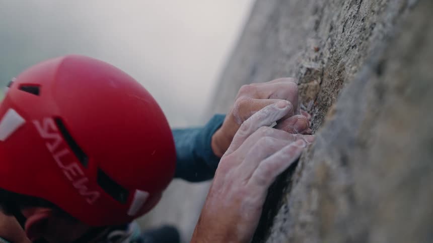 A climber's chalk-covered hands find a secure grip on a rugged cliff face in a dramatic close-up
