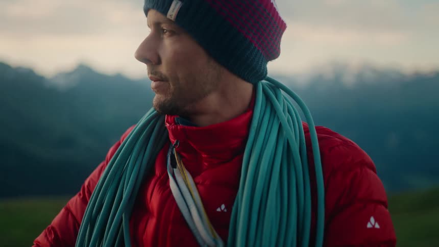 A mountaineer in a red jacket carefully prepares his climbing rope in a beautiful mountain landscape at dusk
