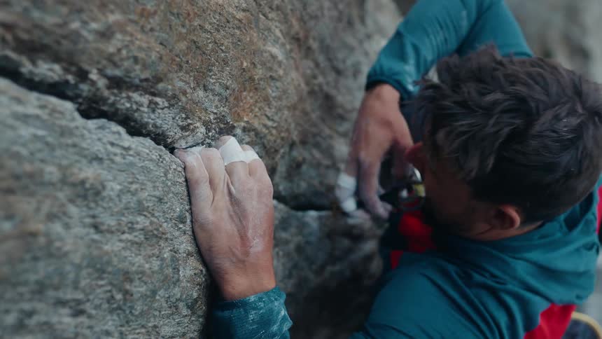 A focused male trad climber with chalked hands places protective gear into a granite rock crack in slow motion